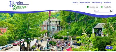New Eureka Springs, Arkansas website with text and icons in royal blue and kelly green colors. An image of Downtown Eureka surrounded in lush green foliage.